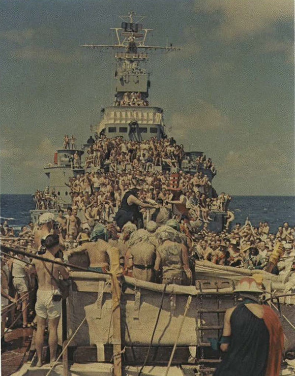 A ship at sea with hundreds of soldiers on deck.