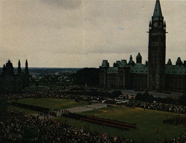 Hundreds of people on the lawn of Parliament Hill, and soldiers marching.