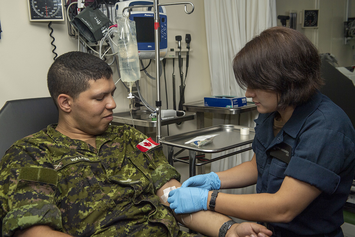 Un médecin militaire prépare un membre des FAC à recevoir une intraveineuse dans le cadre d’une formation.