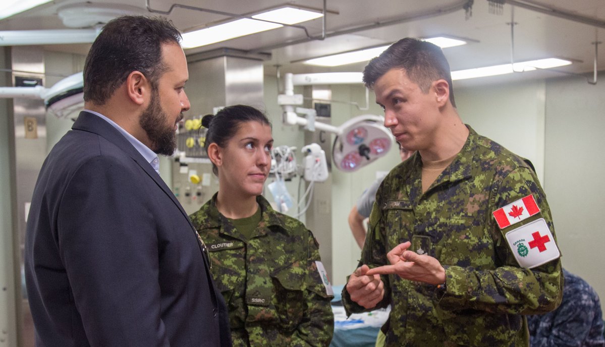 Two Canadian military members are talking to a civilian on board a ship.