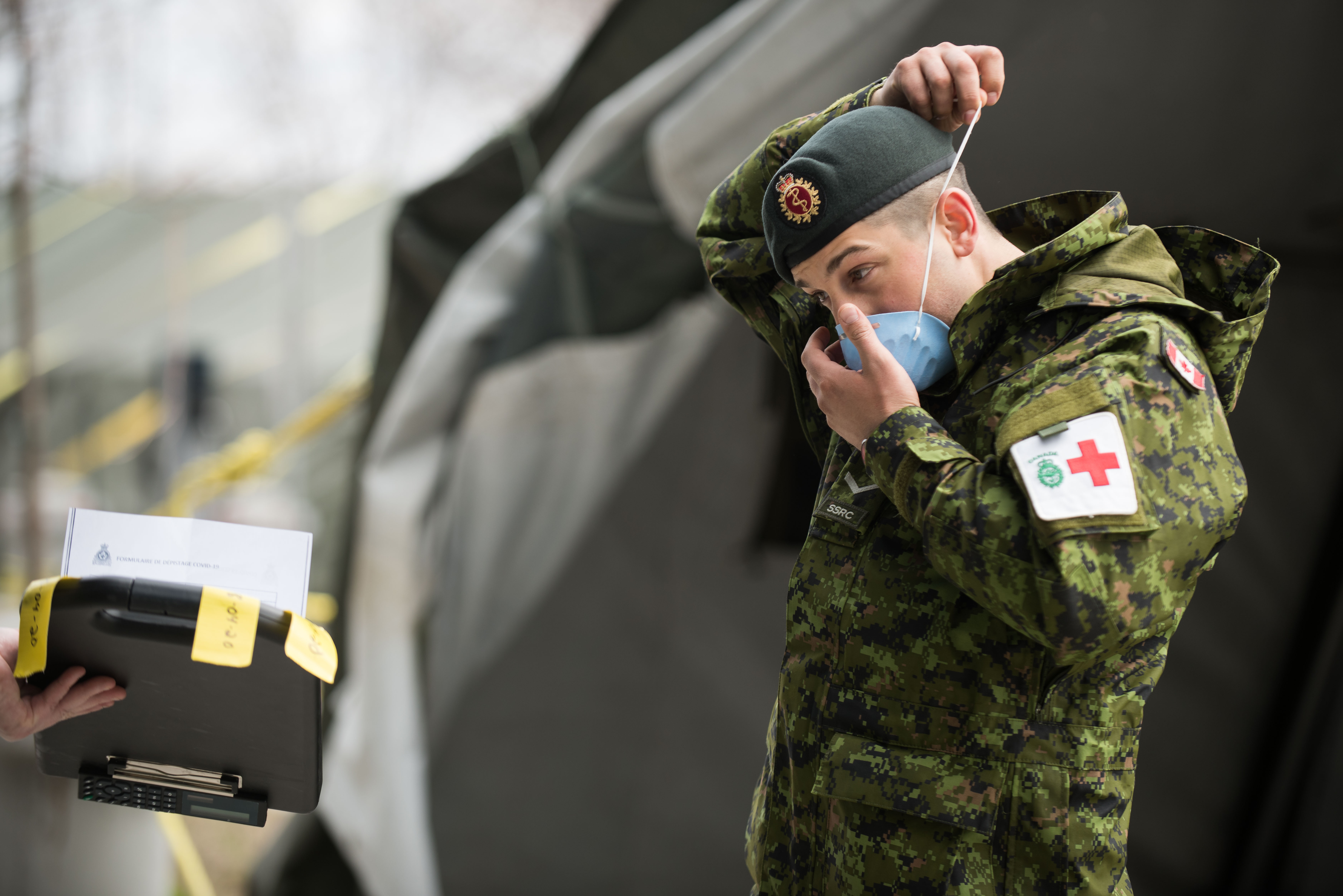 Un membre du 4e Groupe des services de santé (4 Gp Svc S), procède à un triage pour pouvoir entrer dans la clinique de la garnison Saint-Jean afin d’y recevoir une formation durant l’Opération LASER le 18 avril 2020. Photo : Caméra de combat des Forces canadiennes