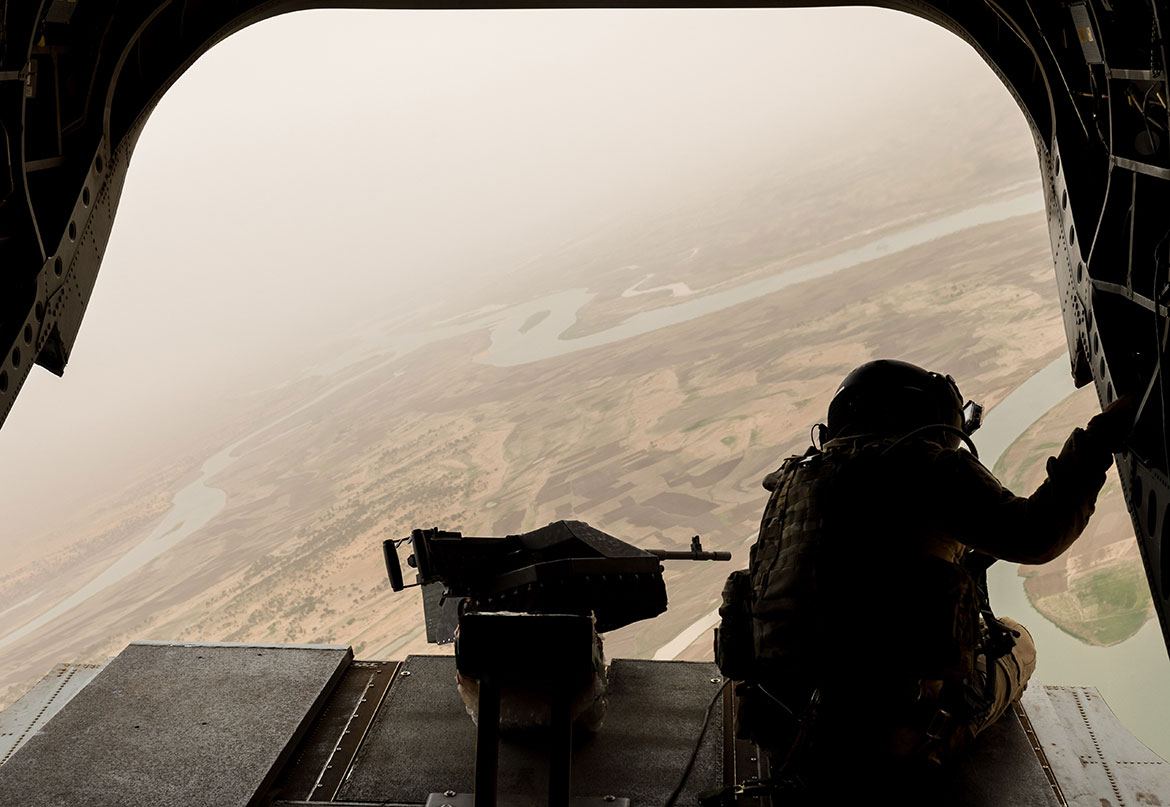 A soldier looks out at the view from the mouth of an aircraft.