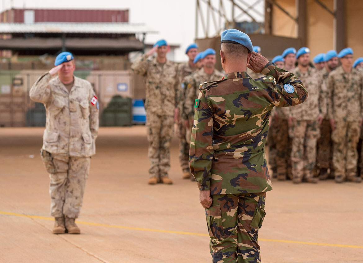  Deux militaires se saluent pendant qu’un groupe de militaires se tiennent debout en formation.