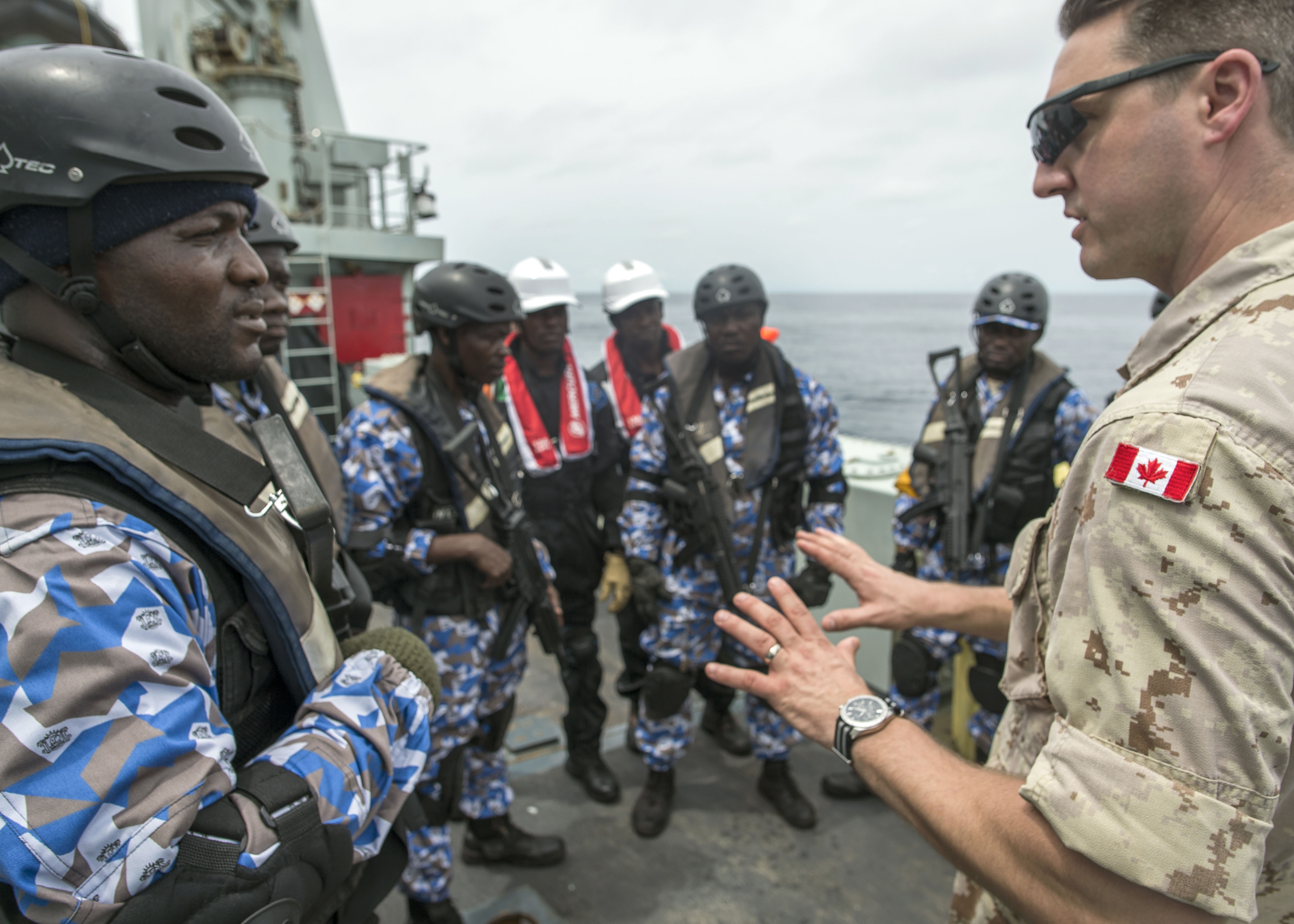25 mars 2018. Le capitaine de corvette Drew Foran, agent de liaison au Centre des opérations maritimes en Côte d’Ivoire, discute avec les membres de l’équipe d’arraisonnement de la Côte d’Ivoire dans le cadre de l’exercice naval OBANGAME EXPRESS, à bord du NCSM KINGSTON, au cours de l’opération PROJECTION, au large de la côte de l’Afrique occidentale, le 25 mars 2018. Photo : Sgt Shilo Adamson, Quartier général du groupe du recrutement des Forces canadiennes, BFC Borden