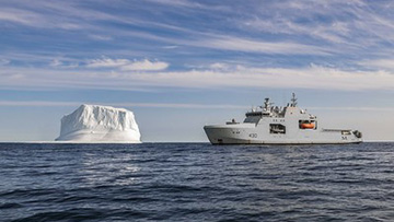 Un navire gris de la Marine royale canadienne, le NCSM Harry DeWolf, est photographié à côté d’un iceberg.