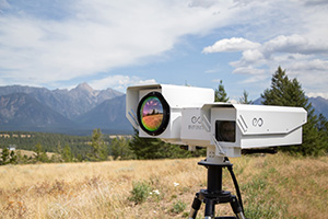 A drone camera on a tripod with trees and mountains in the background.