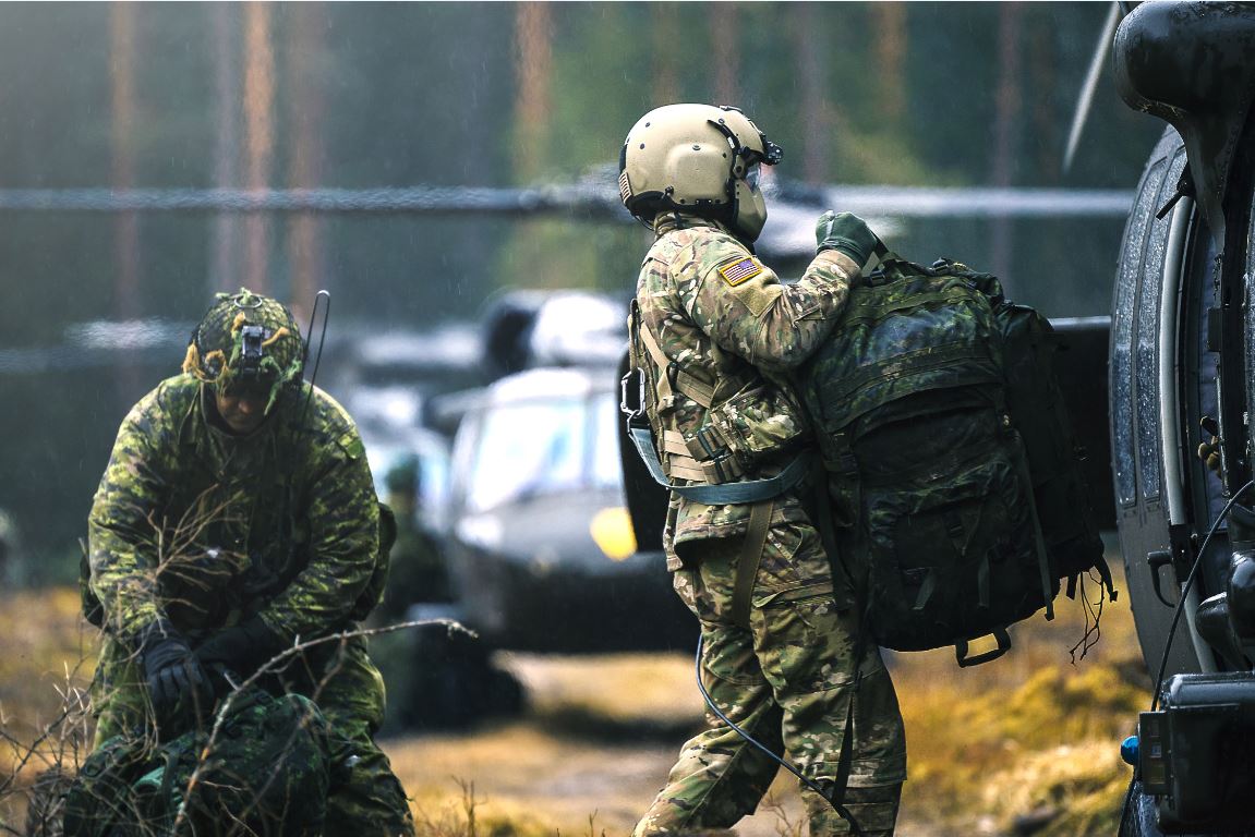 Un membre d’équipage des Forces armées des États Unis aide un membre des Forces armées canadiennes du groupement tactique de la présence avancée renforcée en Lettonie à charger des sacs à dos à bord d’un hélicoptère UH-60 Black Hawk lors d’une mission de récupération des troupes au cours de l’exercice CLAYMORE SOARING, dans le secteur d’entraînement de Meza Mackavici, dans le cadre de l’opération REASSURANCE, le 6 avril 2018. Photo : Cpl Desiree T. Bourdon, Force opérationnelle de Lettonie RP16-2018-0029-179