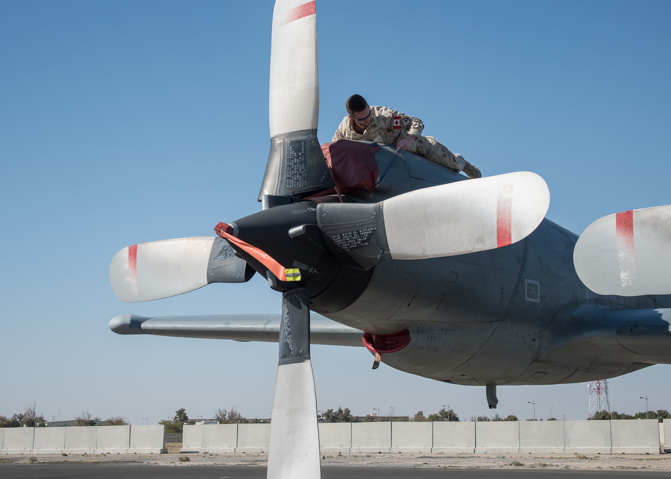 L’image a été modifiée numériquement pour des raisons de sécurité opérationnelle.  19 février 2017. Un technicien en avionique de la Force opérationnelle aérienne – Irak (FOA-I) installe un couvert de protection sur la trappe d’admission de l’hélice d’un aéronef CP-140 Aurora au cours de l’opération IMPACT, le 19 février 2017. (Photo : Op Impact, MDN) 