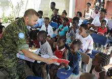 Port-au-Prince (Haïti). 18 octobre 2009 – Le Capitaine de corvette Shekhar Gothi, officier des plans et des opérations de la Mission des Nations Unies pour la stabilisation en Haïti (MINUSTAH), remet des livres aux enfants de l’orphelinat (Compassion Orphanage), situé aux abords de Port-au-Prince, en Haïti. (Photo : Caporal Shilo Adamson, Caméra de combat des Forces canadiennes)