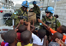 Port-au-Prince (Haïti). 16 septembre 2013 – Le caporal Marc-Daniel Benoit (à gauche) et le sergent David Lapalme (à droite), tous deux issus du 2e Bataillon, Royal 22e Régiment, offrent des vêtements et des accessoires à des enfants haïtiens, le dans le cadre de l’opération Hamlet. (Photo : Cplc Marc-Andre Gaudreault, Caméra de combat des Forces canadiennes)