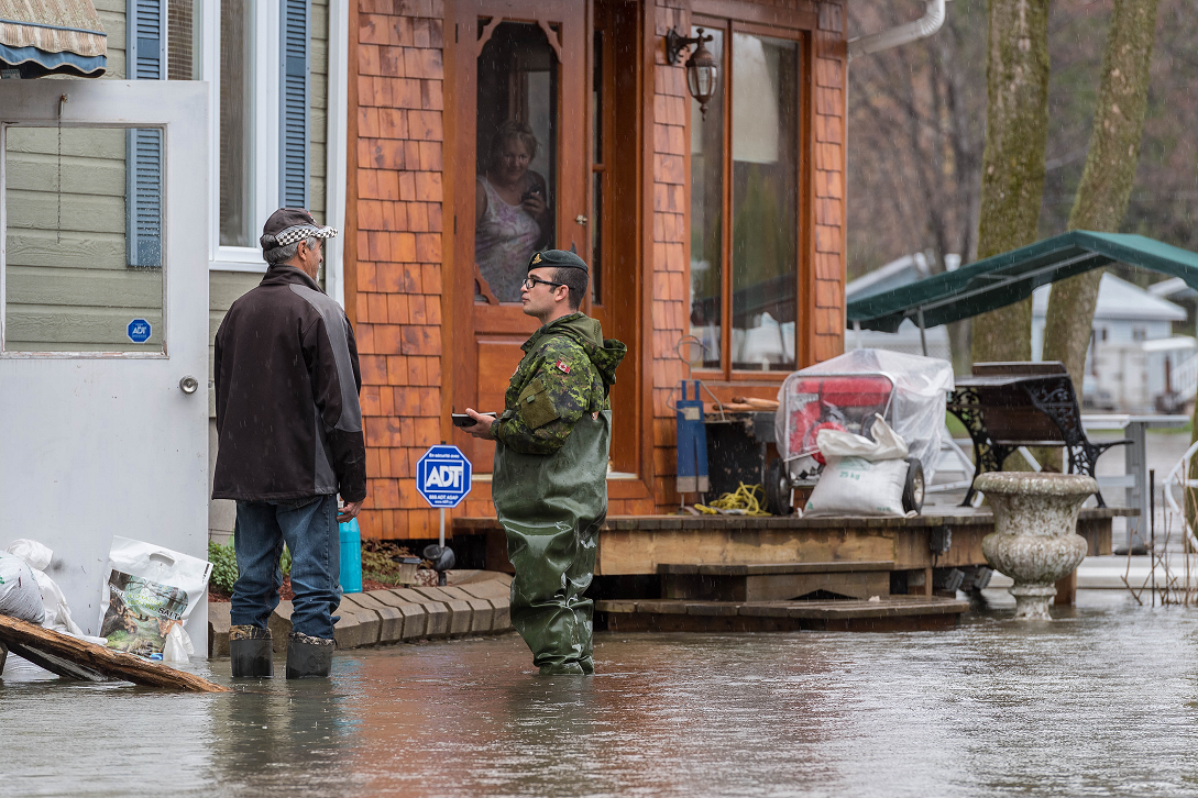 Bombadier Keven Guillette from 5e Régiment d'artillerie légère du Canada talks to residents affected by flooding while assessing the situation of a community in Bécancour, Quebec during Operation LENTUS on May 7, 2017.  (Photo: Cpl Nathan Moulton, Imagery Valcartier)
