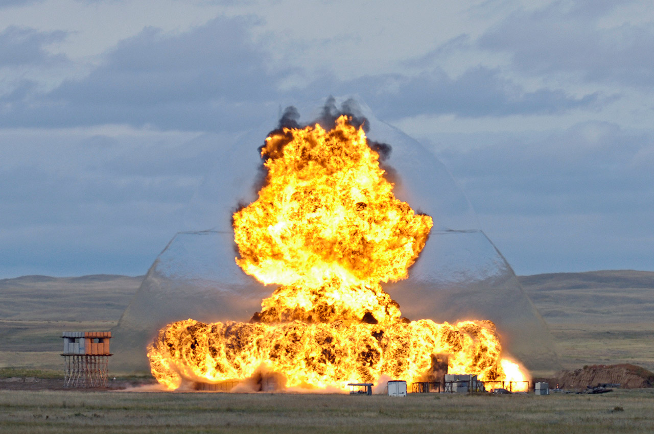 A large burst of flames and shock wave engulfs a series of concrete structures built for an explosives trial on the Experimental Proving Ground at DRDC – Suffield Research Centre. 