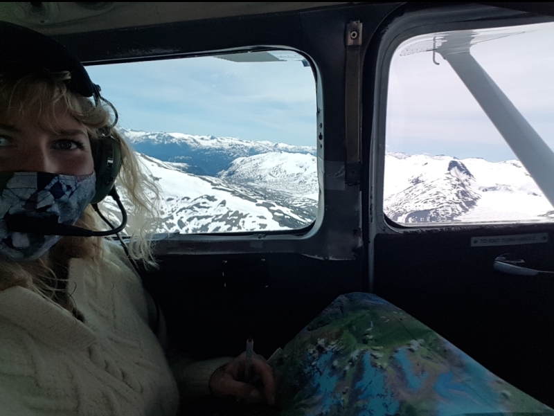 Agnieszka is in a plane during fieldwork, with the backdrop of snowy mountain views.