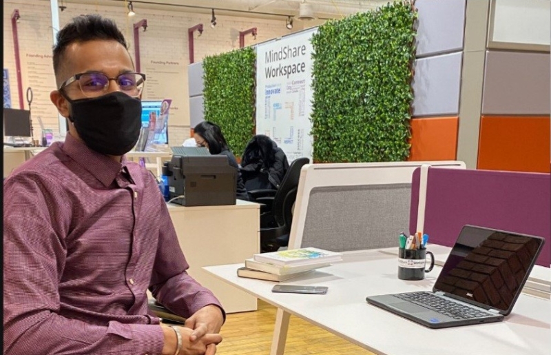 Aman wearing a mask sitting at a desk in front of a laptop.