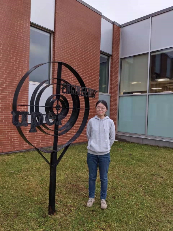 Yulin in front of the University of Prince Edward Island next to a sculpture.