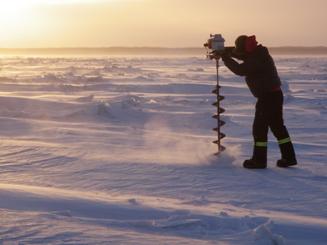 Un technicien en hydrométrie d'ECCC perce la glace du fleuve MacKenzie gelé pour mesurer le débit de l'eau sous la glace.