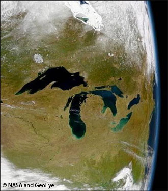 Image satellite des Grands Lacs vus depuis l’espace. La zone terrestre apparaît en vert sur l’image et des nuages blancs bordent le haut et le bas de la photo. Source : © NASA et GeoEye.