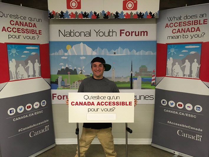 Photo 3: Picture depicts a man holding a sign that asks "What does an Accessible Canada"