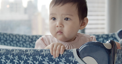 A baby stands and looks over the side of a playpen