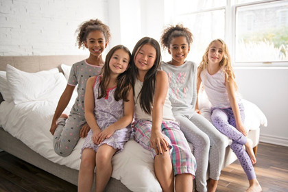 Five children sit on a bed wearing sleepwear
