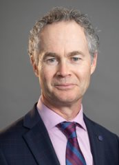 Professional headshot photo of Éric Landry, wearing a pink shirt, striped tie, and back blazer against a neutral gray background.