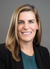 Professional headshot photo of Patricia Brady, smiling, wearing a turquoise shirt and a black blazer against a neutral gray background.