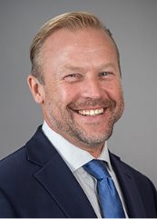 Professional headshot photo of Terence Hubbard, smiling in business attire against a neutral gray background.