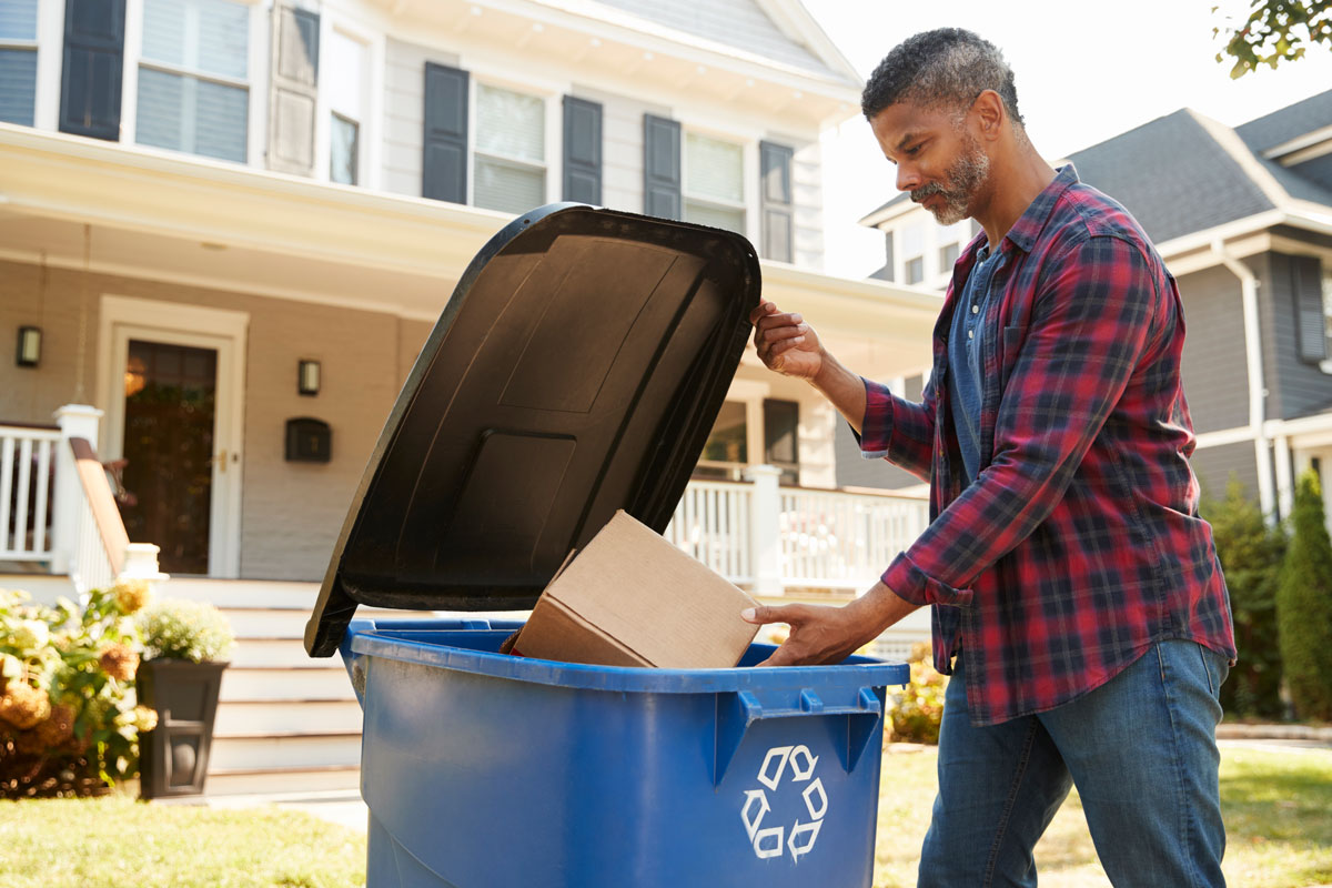 Homme mettant une boîte en carton dans un bac de recyclage