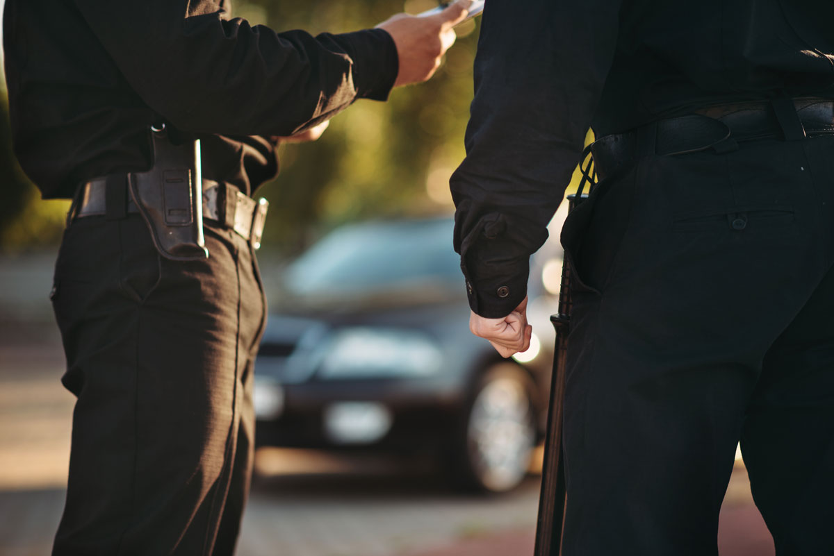 Vue de deux policiers à la hauteur de leur ceinture examinant des documents devant leur voiture de police
