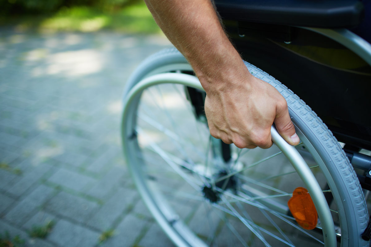 Gros plan de la main de la personne à mobilité réduite sur la roue de son fauteuil roulant