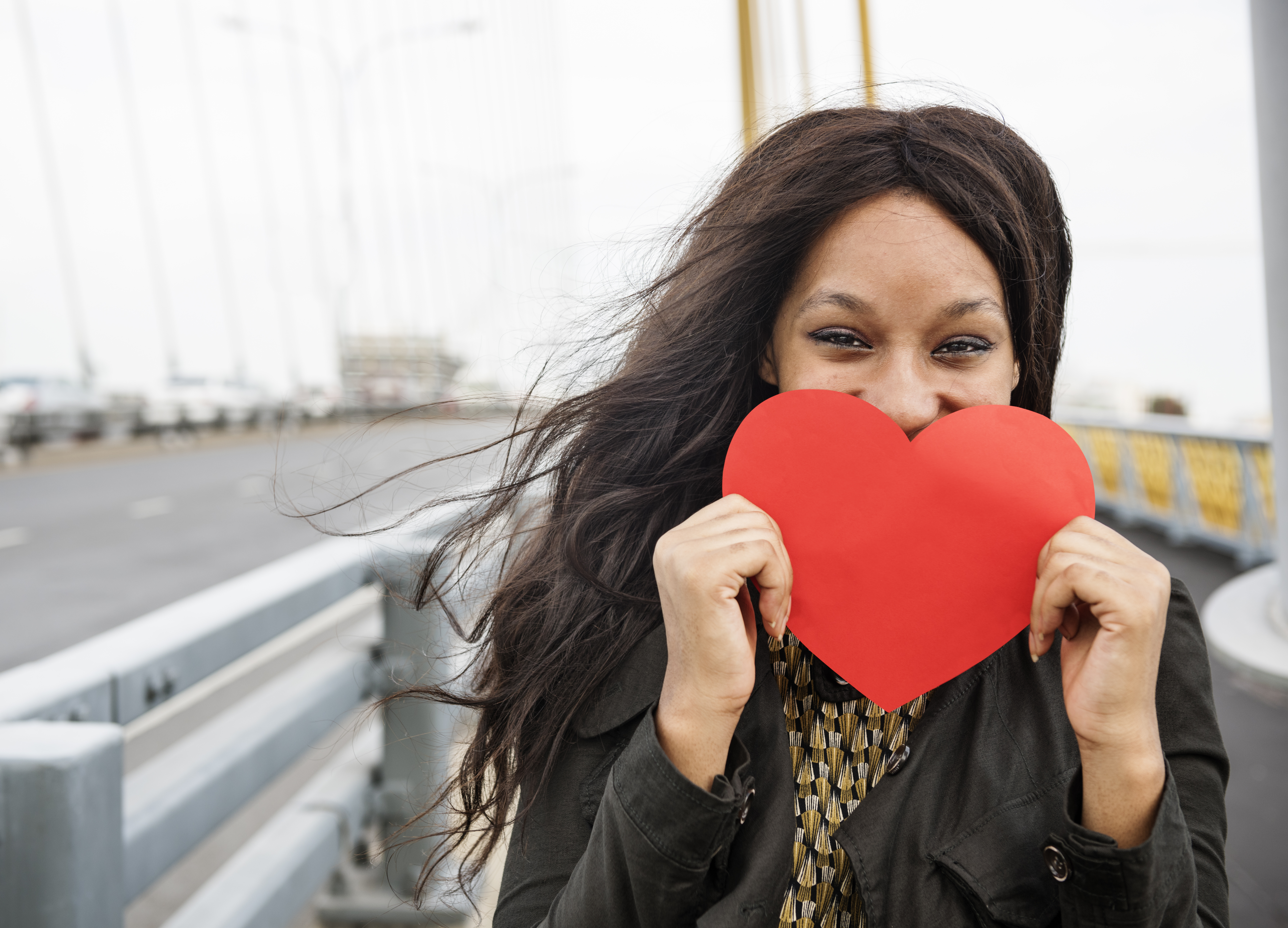 Woman holding a paper cut-out of a stylized heart in front of her face