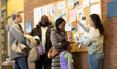 Four adults and a child engage in conversation and stand in front of a bulletin board.