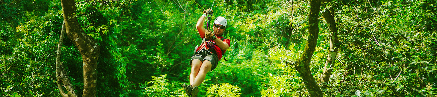 A person zip lines through bright green trees in Costa Rica