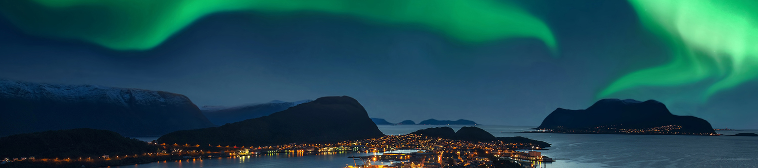 An aerial view of a city in Norway at night with the Northern Lights in the background