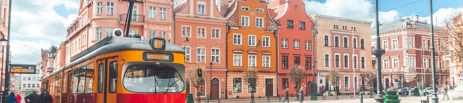 Un tramway arrive dans une station devant une rangée de bâtiments roses et orange en Pologne.