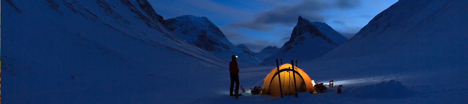 Une personne à côté d’une tente dans les montagnes en Suède, la nuit