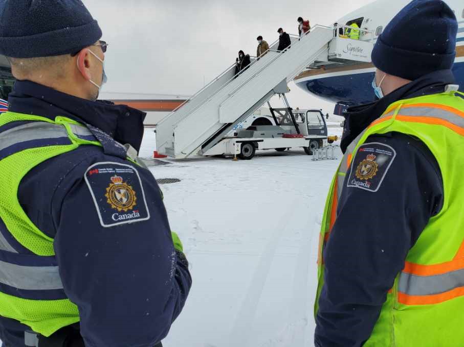 Deux agents de l’ASFC regardent des réfugiés afghans parrainés par le secteur privé sortir d’un avion à Toronto, le 8 décembre 2021.