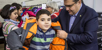 Denis Coderre, Mayor of Montreal, helps a child put on a winter jacket.