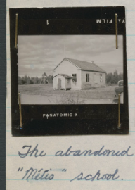 Photographie en noir et blanc sur une page gris clair avec une légende manuscrite à l’encre bleue en dessous.