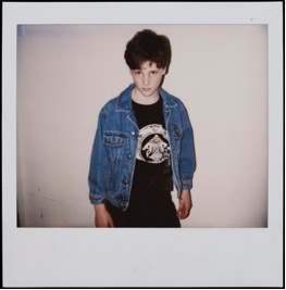 Garçon vêtu d'une veste de denim et d'un t-shirt noir orné d'inscriptions.