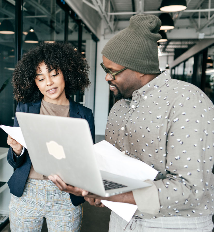 Deux personnes qui travaillent et discutent, un ordinateur portable et des papiers à la main.