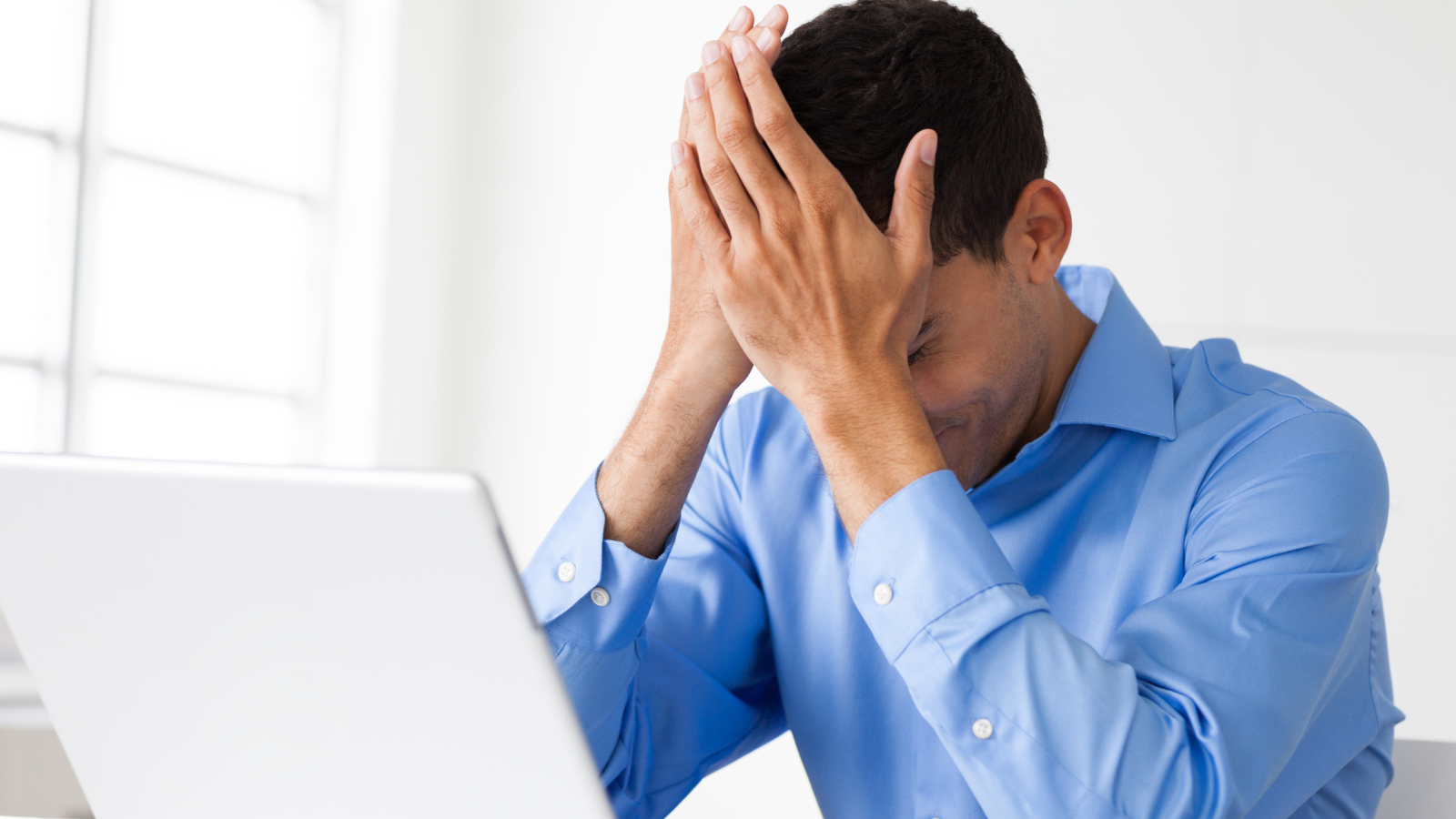 man frustrated with hands on head looking at his laptop