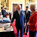 Prince of Wales pointing at a knitted shirt and speaking with a representative of Campaign for Wool.