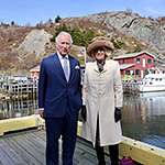 Prince of Wales and Duchess of Cornwall standing on wharf with small village of Quidi Vidi in background.