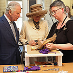 Prince of Wales and Duchess of Cornwall watching and learning about the art of rug hooking.