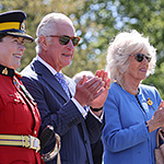 Prince of Wales and Duchess of Cornwall applauding and smiling, next to a member of the RCMP