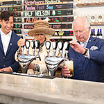 Prince of Wales and Duchess of Cornwall behind bar pouring draft beer.