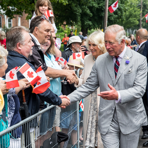 The Prince of Wales and Duchess of Cornwall greet crowd of people waving Canadian flags.