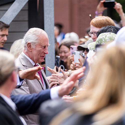 Le roi Charles III et la reine Camilla saluent un groupe de personnes en leur serrant la main lors d'un rassemblement communautaire.