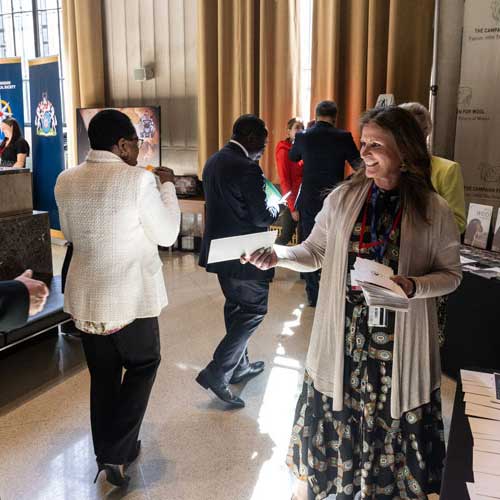 A woman distributes envelops to guests in front of the information booths.